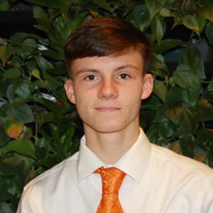 Liam Ward, wearing an orange tie and white shirt, poses against a green backdrop.