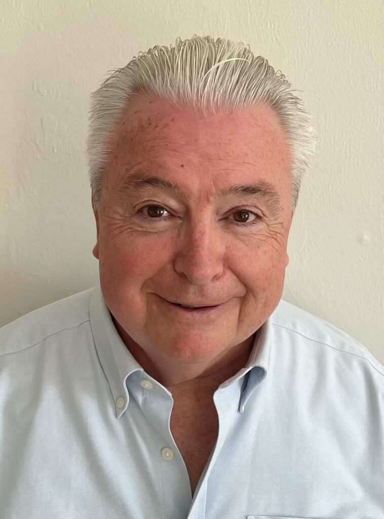 Glenn Connell portrait, smiling man with silver hair wearing a light blue shirt.