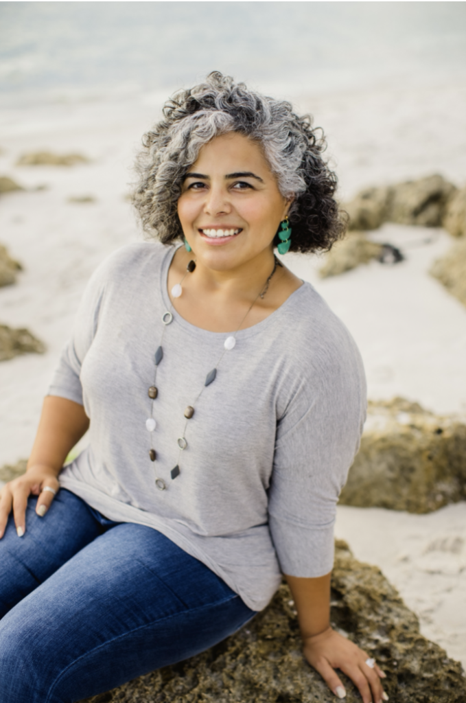 Yesenia "Jessie" Pedraza smiling on a beach with curly hair and turquoise earrings.